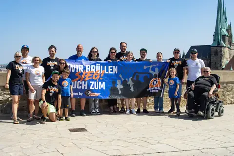 Große Fangruppe hält das Banner „Wir brüllen euch zum Sieg“ hoch