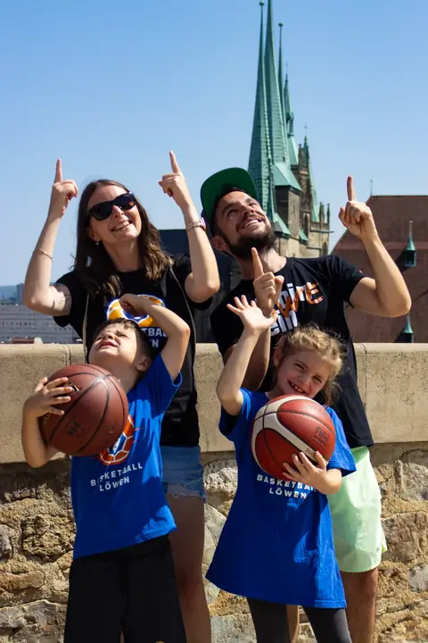 Zwei Kinder mit Basketbällen, dahinter die Eltern mit Daumen nach oben