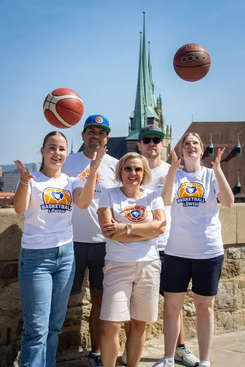 Fans in weißen Löwen-Shirts jubeln, ein Basketball fliegt über ihnen